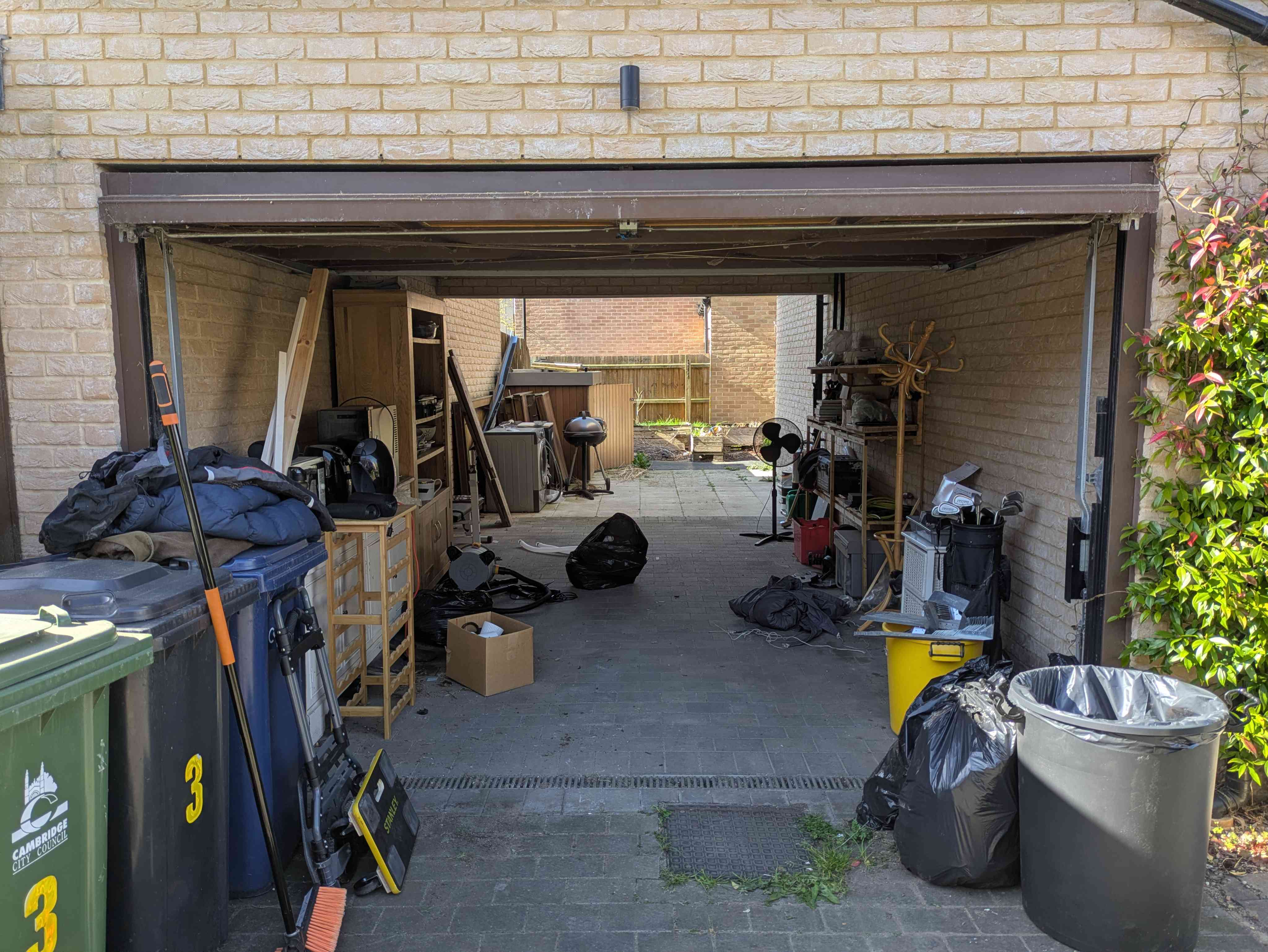 A double garage with belongings stacked across the floor and out toward the driveway