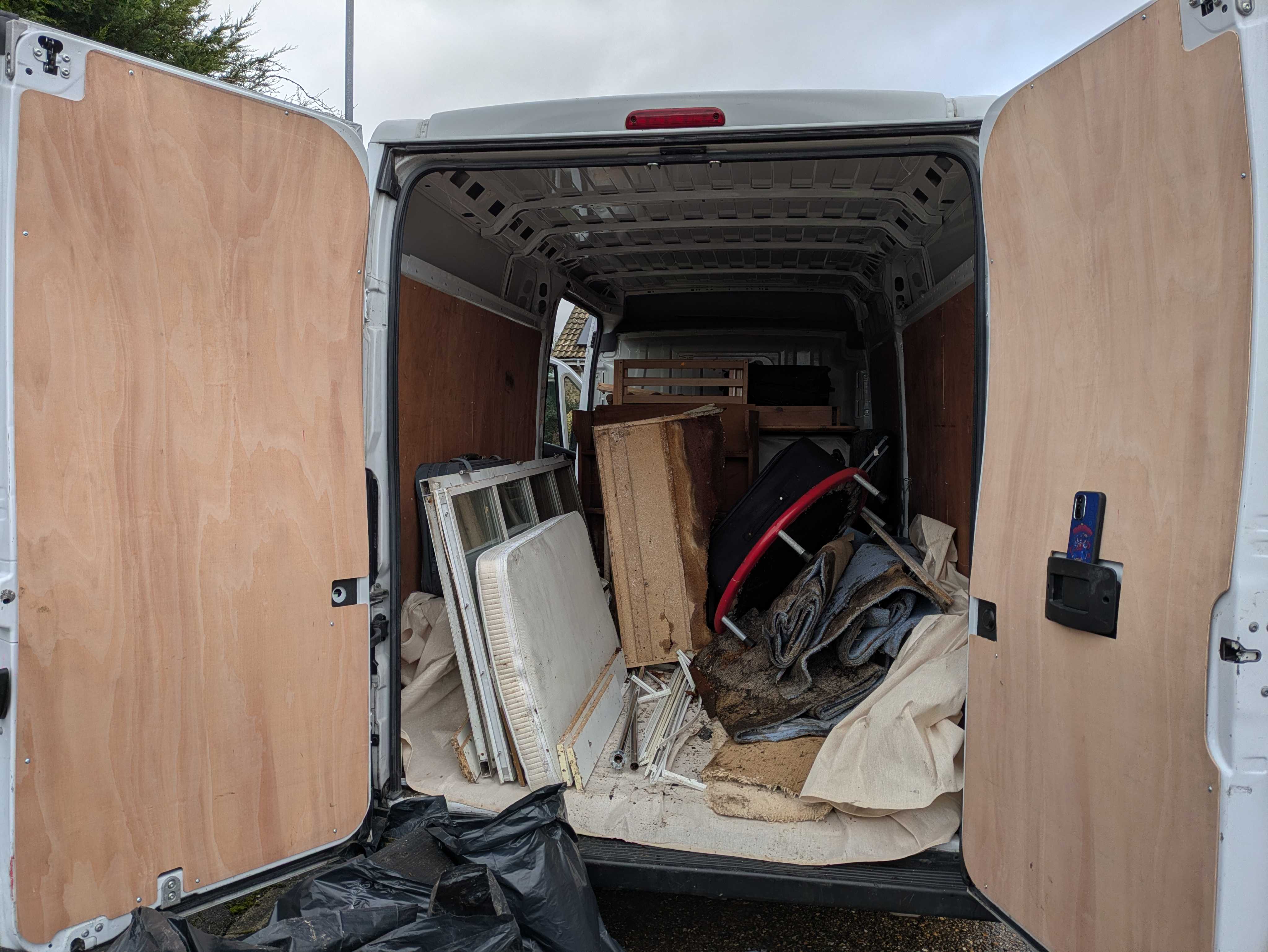 Inside the open back doors of the van — bathroom suite, bagged carpet and offcuts loaded for the tip and recycling run